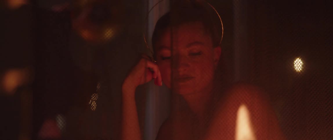 Young woman sitting behind a curtain veil looking at a fire at night