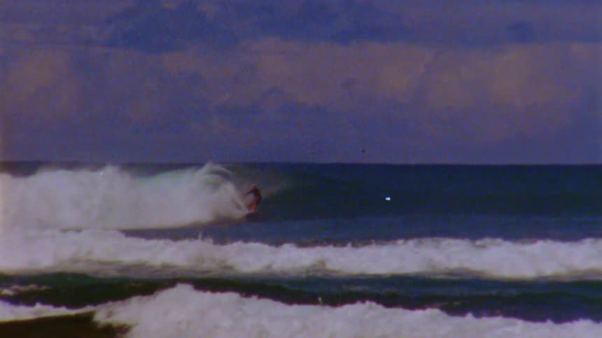 Waves crashing against the shores while a surfer rides a wave and then crashes