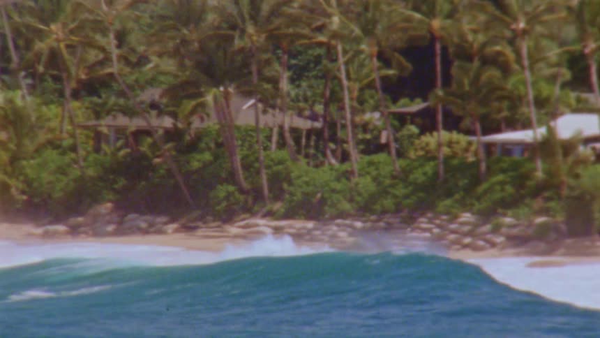 Blue waves crashing onto a sandy beach with buildings in the background