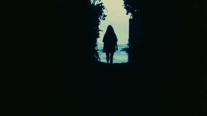 Woman with shirt and shorts walking down the beach near the ocean is silhouetted agains the sky