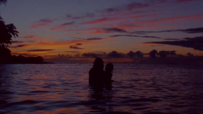 A silhouetted mother and infant swimming in the ocean at dusk