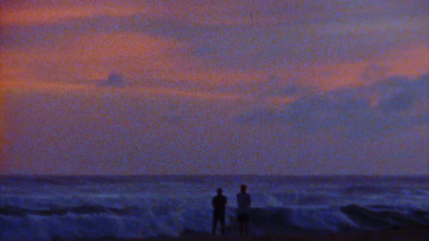 Two people stand on the beach at sunset