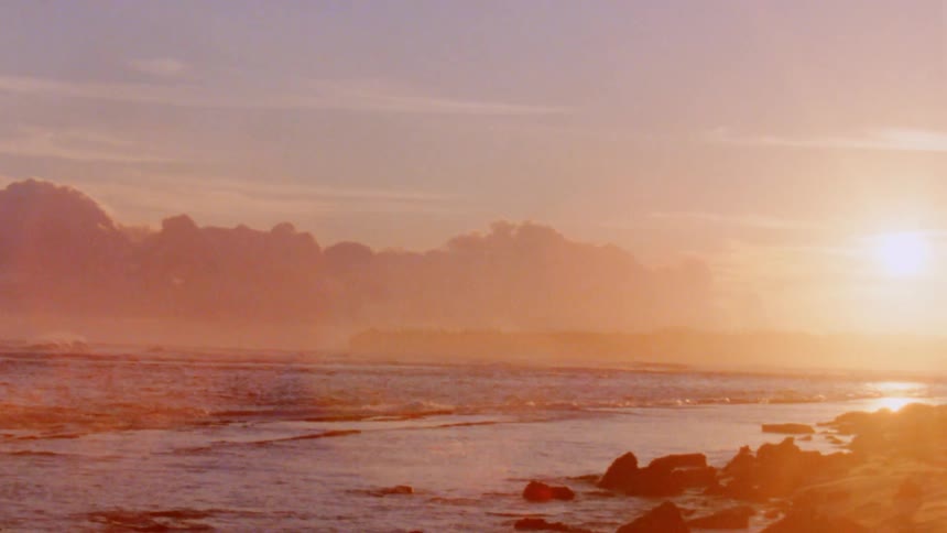Ocean waves wash into a rocky beach under a low evening sun