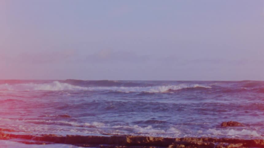 Small calm ocean waves gently crashing on the coast at evening caught on vintage film