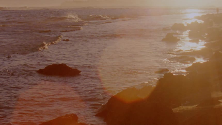 Landscape of ocean waves breaking against rocky shore at sunset