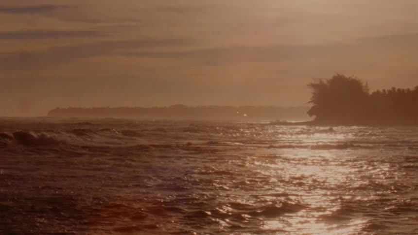 Slow motion footage of golden sunlight reflecting over the waves near the tropical coast