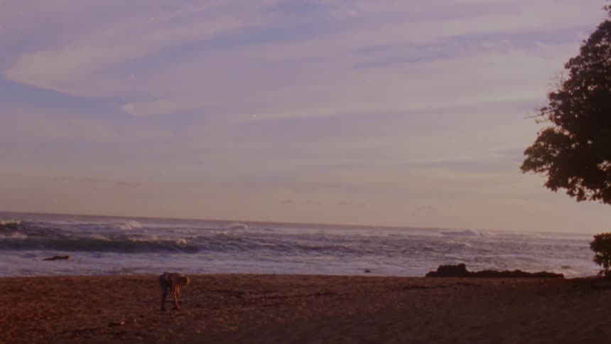 A person standing and bending over on a beach at sunset