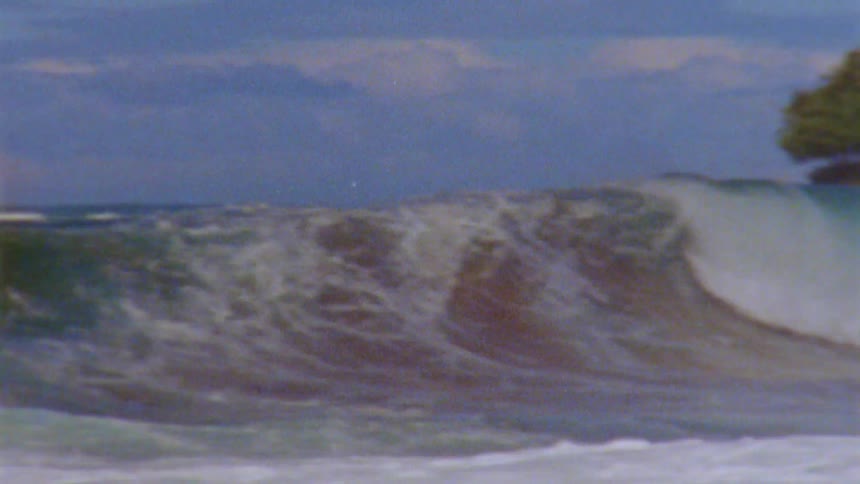 A big wave rolls into shore under a cloudy sky