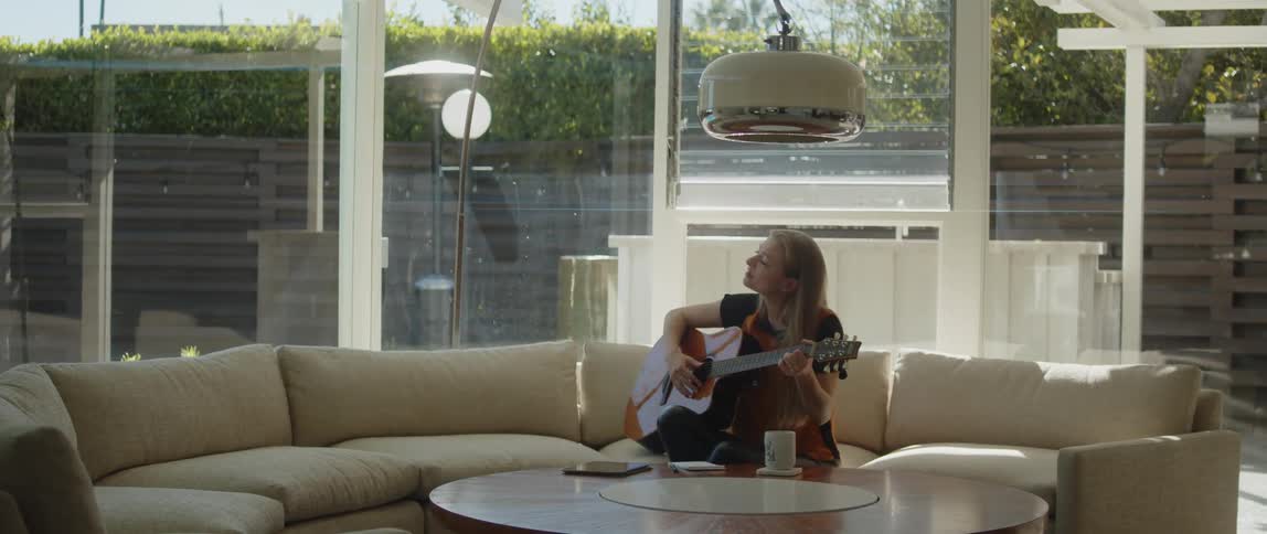 A woman playing a guitar while sitting on a living room sofa