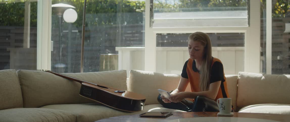 A young white woman by her guitar on a beige couch during the day