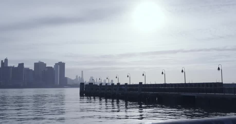 Placid view of the calm surface of the ocean near a pier close to the city skyline at evening