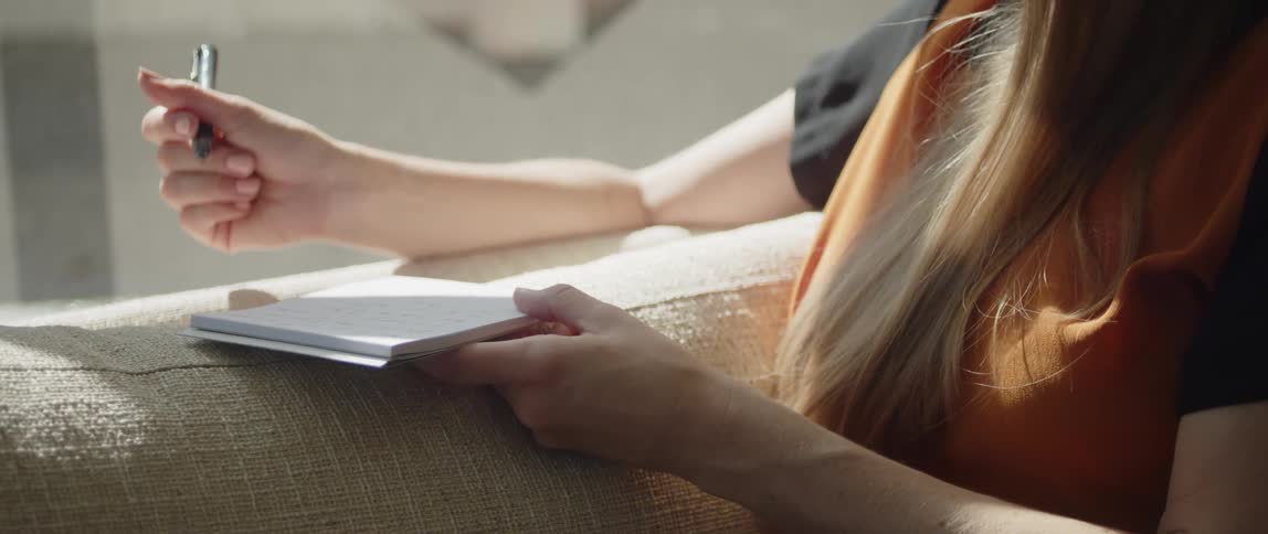 A woman is sitting on the couch holding a notepad and a pen
