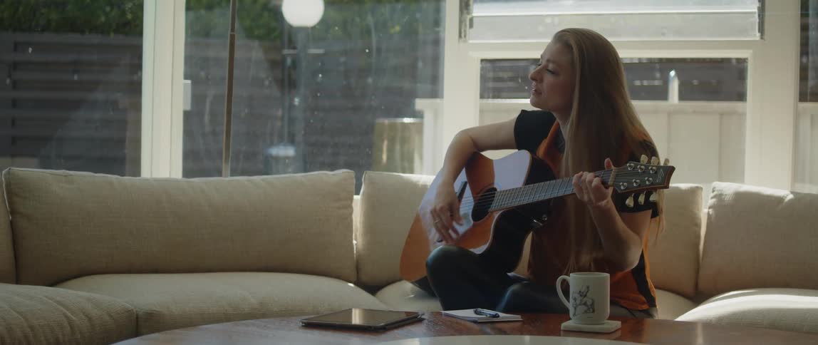 A woman is sitting indoors and playing the guitar