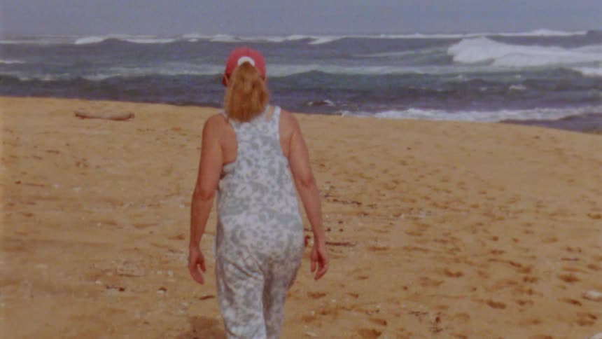 There is a older white woman that is walking down on the beach