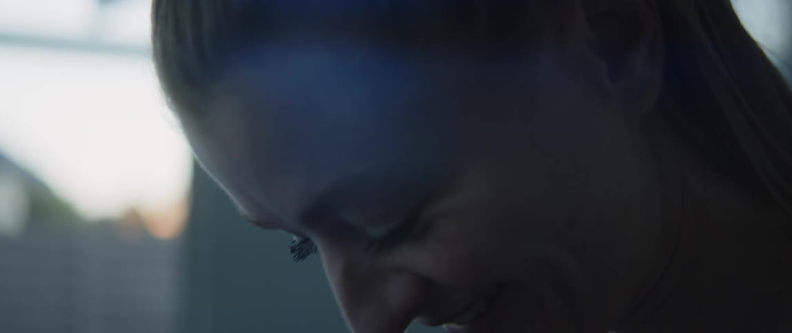 Side profile of woman with brown pony tail and black t shirt looking down and smiling