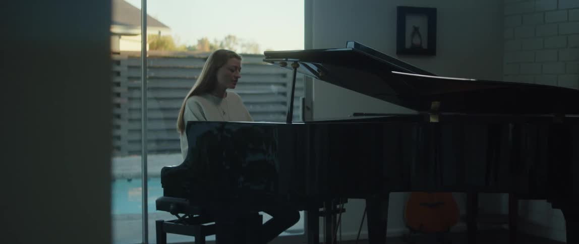 Woman wearing a white sweater playing the piano while singing