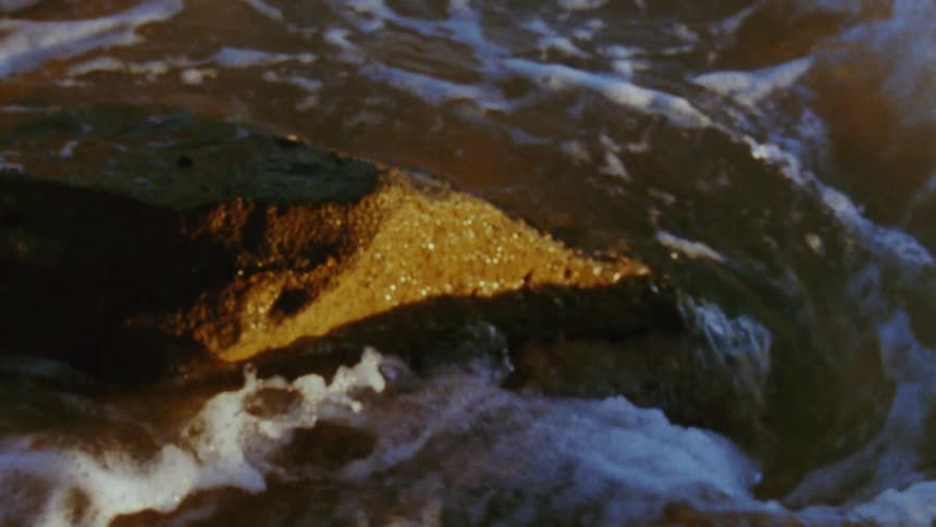 Waves wash around a rock on a beach during the day