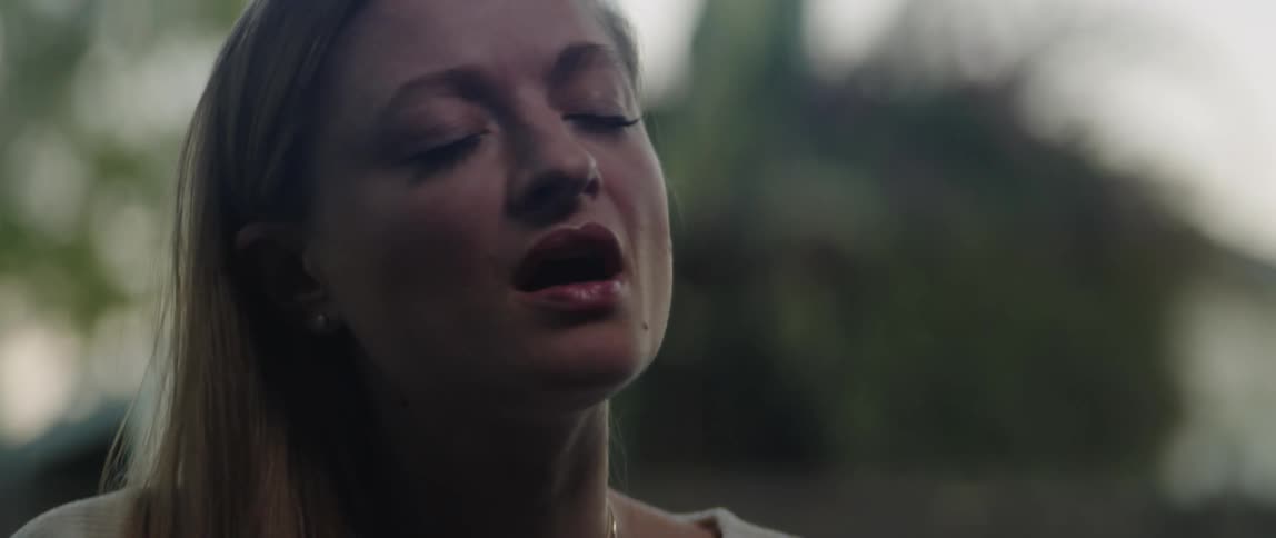 A blonde woman with pink lipstick singing with her eyes closed