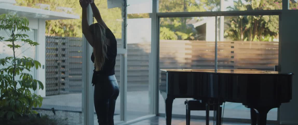 Woman with ponytail black shirt and pants does yoga next to grand piano in room at home