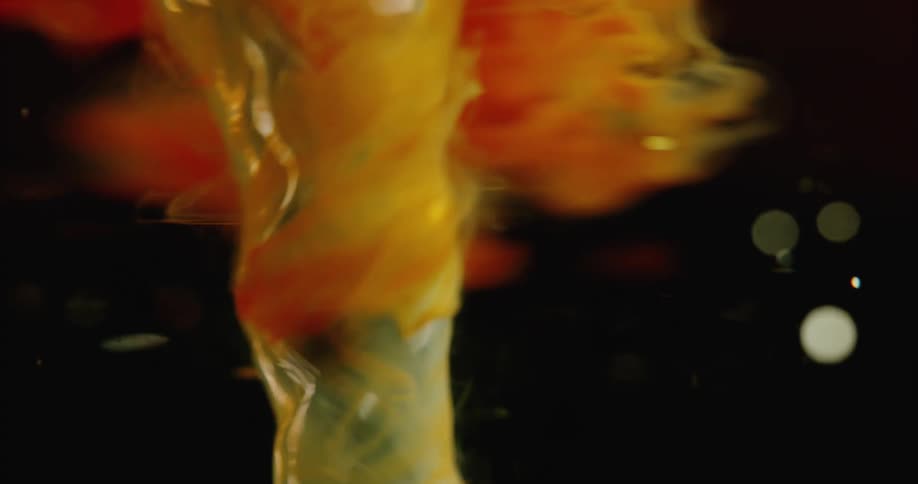 Orange dye flows down and wraps around vortex as reflective disks float through translucent fluid