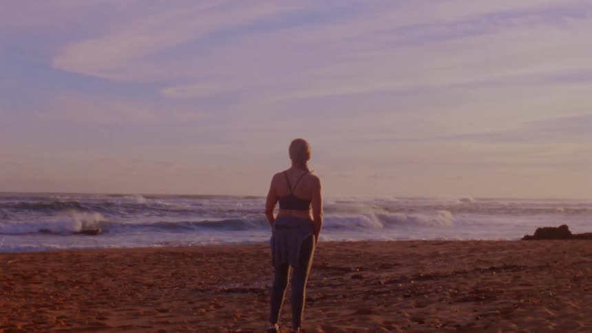 The white woman is standing on the beach and looking at the ocean