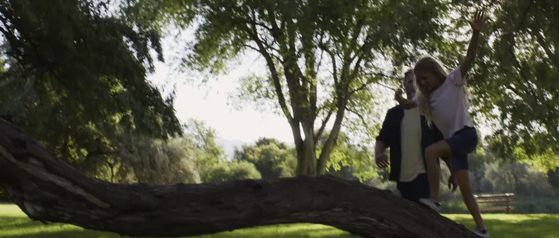 Father in black and white shirt and pants chases daughter in green public park