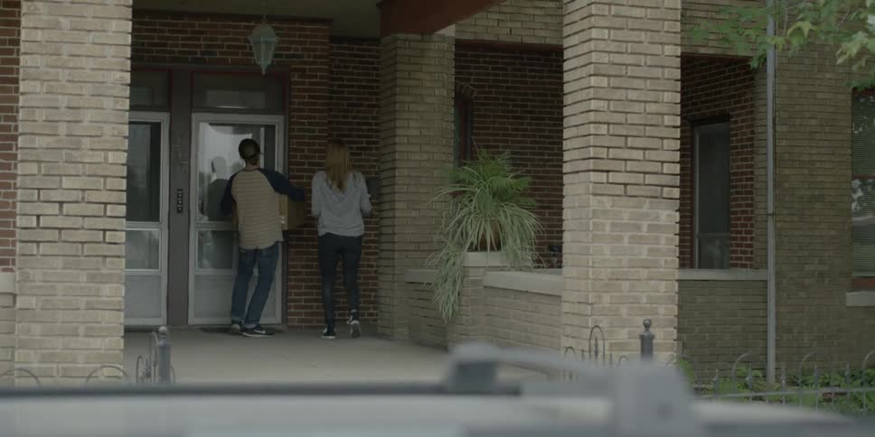 Two people walk up to a door, one person holding a box opens the door