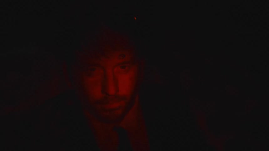 Close up of the face of a bearded man submerged underwater under flashing red lights
