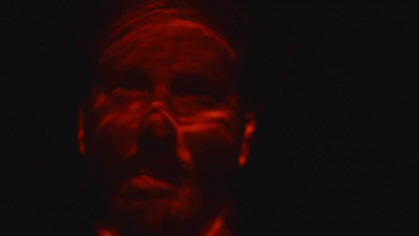 A red light shines over a mans face while he floats underwater