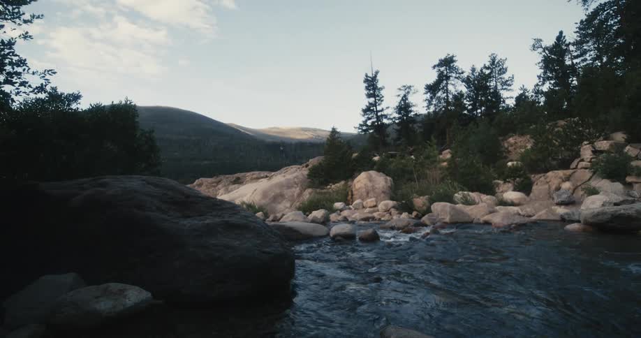 River flows past boulder strewn banks with mountains in the background