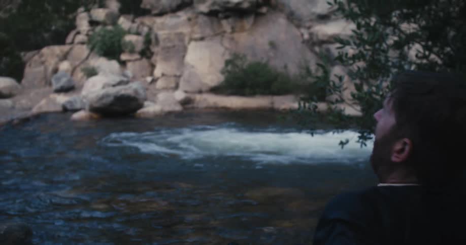 Young bearded man wearing a business suit desperately crawls out of a river