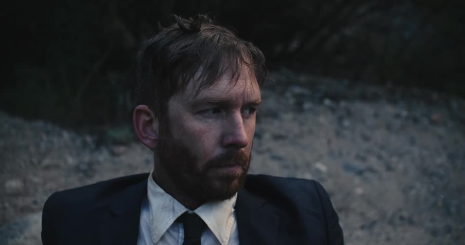 A man is sitting outdoors and looks upset