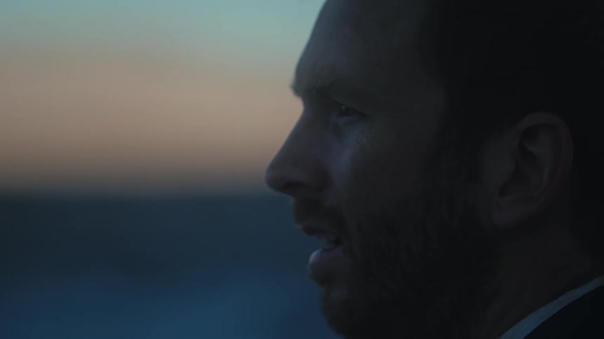 Side profile of man with beard and dirt suit looking around tired and exhausted in open field at dusk