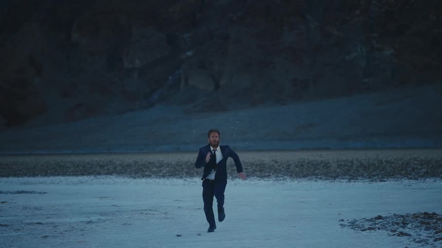 A man in a suit runs through a desert near a canyon