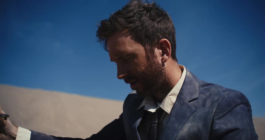 Man with beard and dirt suit checks briefcase in the desert