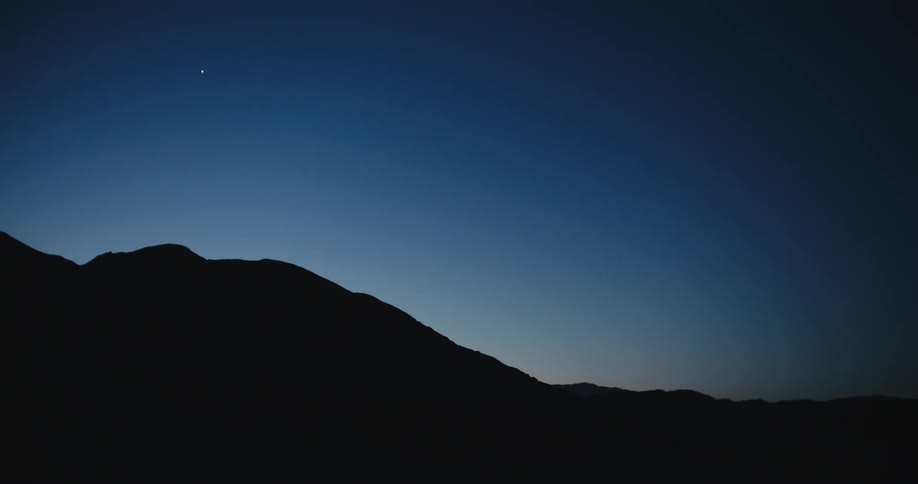 A bright star in a clear sky is about the silhouette of a mountain