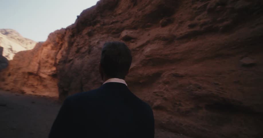 A man walks at the base of a cliff and looks around