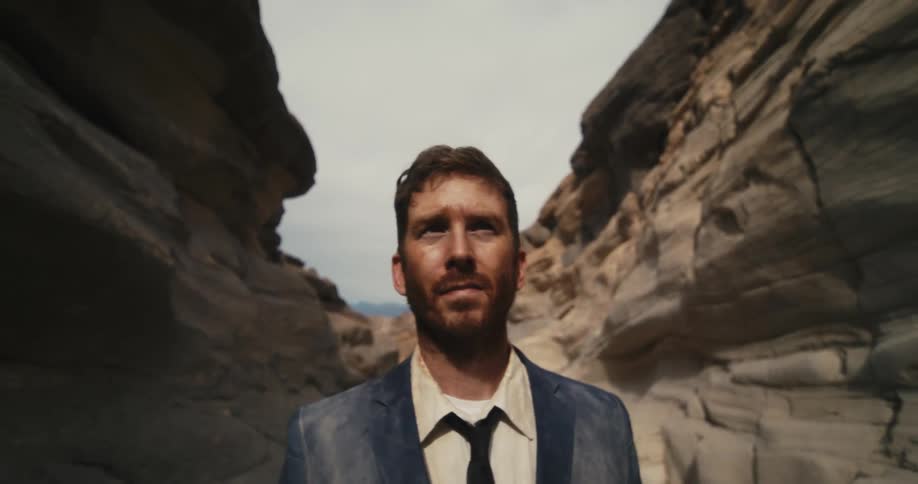 Bearded man walking through a canyon in the desert wearing a business