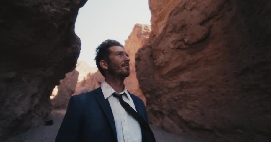 Man wearing suit walks through narrow canyon on windy day