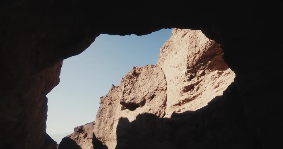 Looking out from a mountain cavern the sun is shining on the mountain rock above