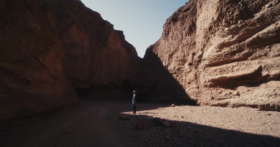A man in a suit looks up at a rock face while standing on the floor of a canyon during the day