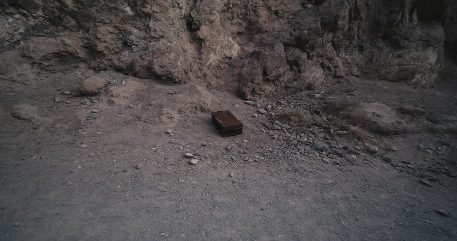 A briefcase is lying on the ground in the desert soil among rocks near a mountain