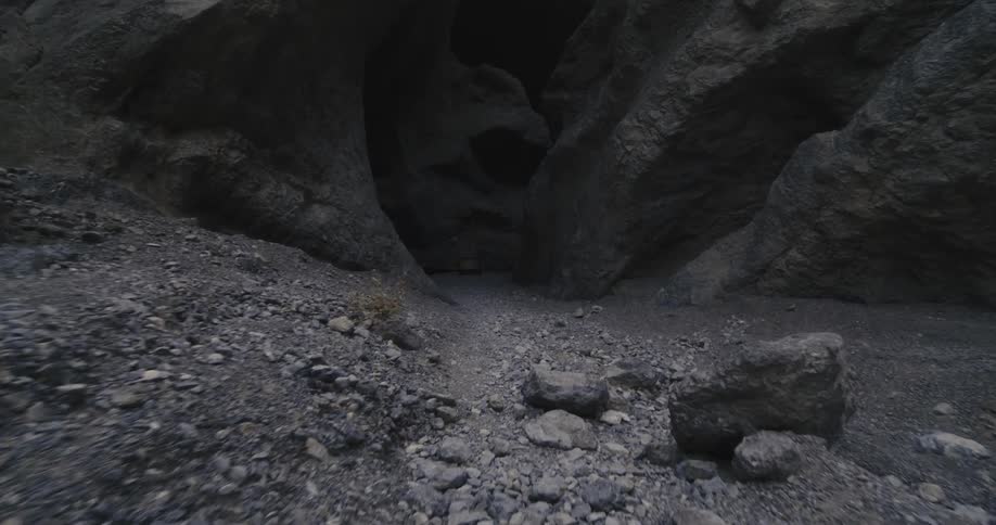 A rock filled path leads to a cave in a mountain