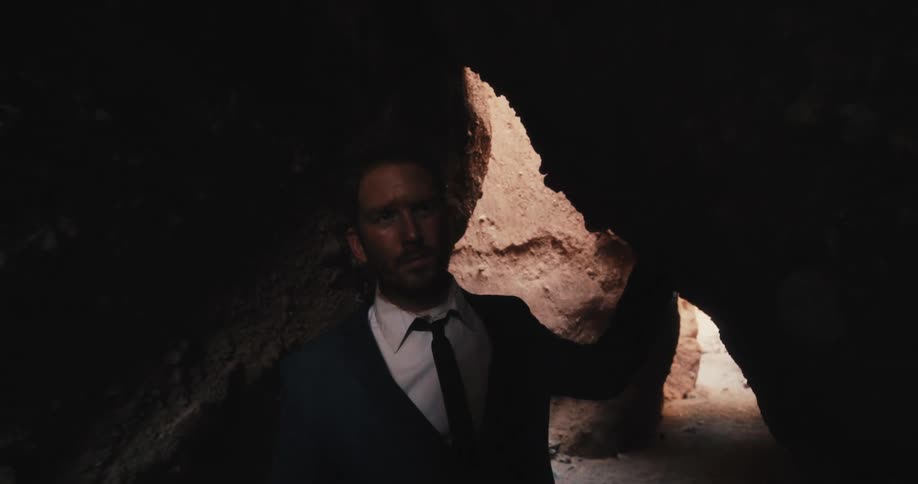 A man in a suit walks through a narrow cave during the day