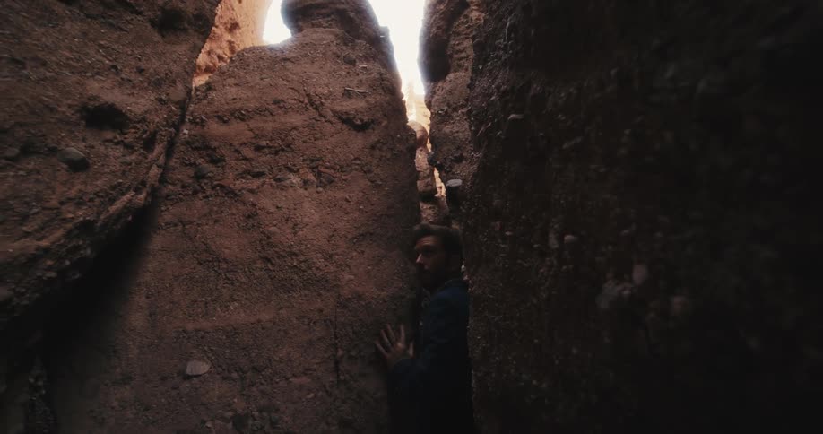 A man in a suit walks sideways through a narrow passage in the rocks