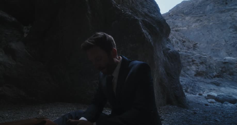 Bearded man sitting in the desert wearing a business suit turns talking to himself