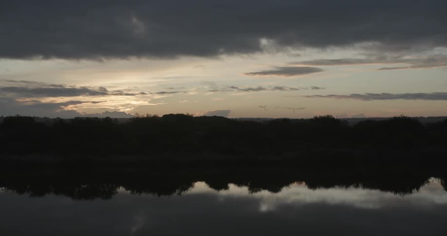 A placid lake reflects the sky and surrounding forest in the evening