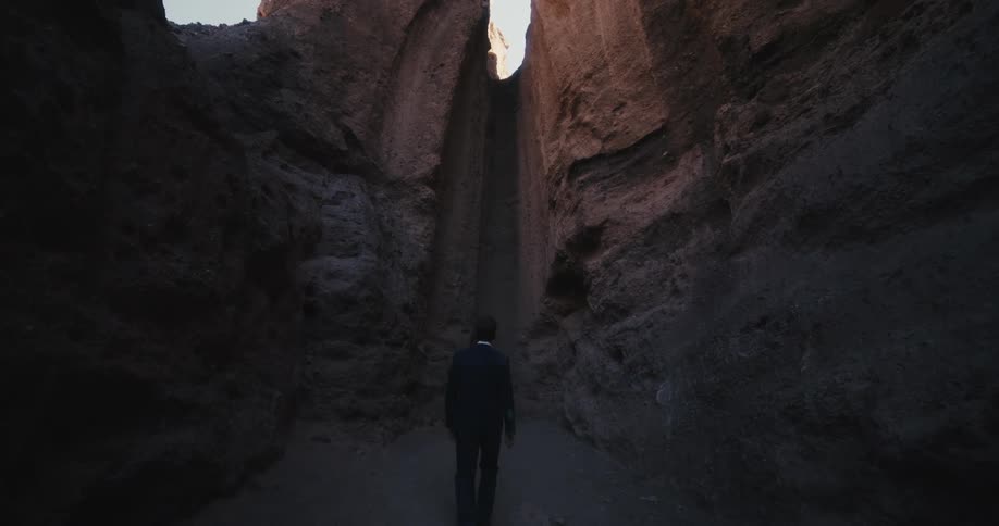 Man walks along canyon toward sleek notch allowing glimpse of clear sky