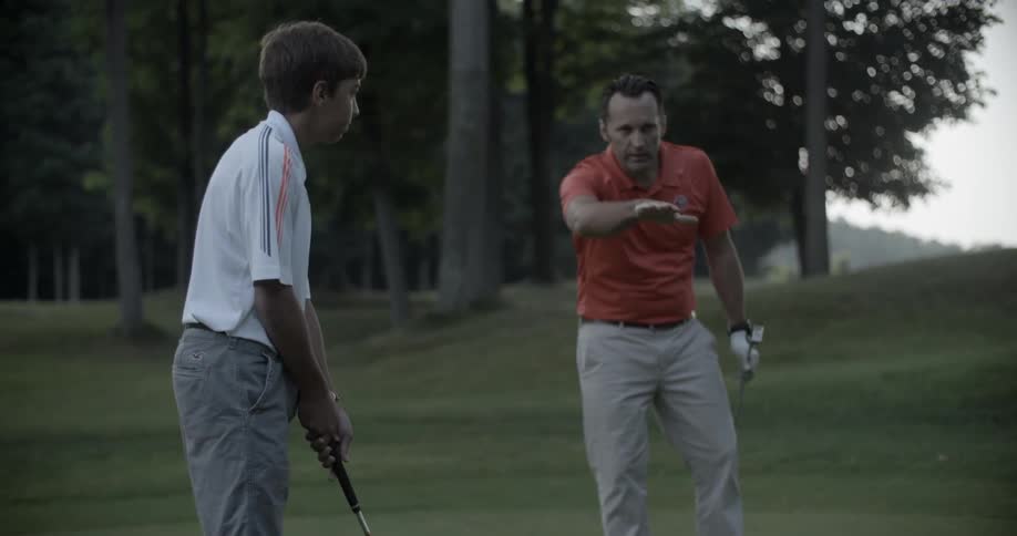 A man is giving pointers to a young golfer
