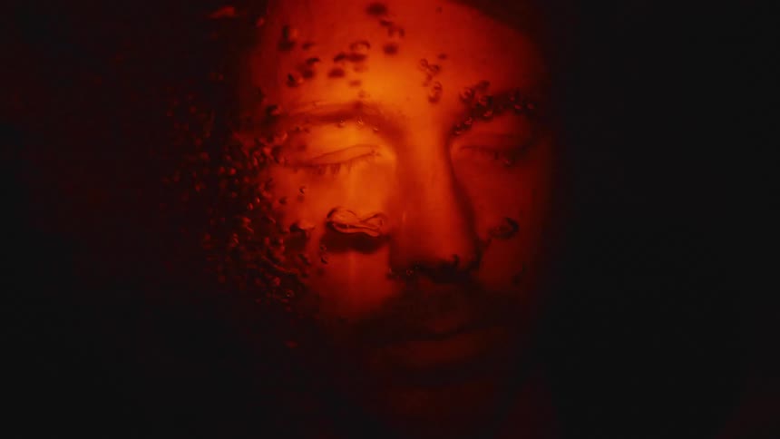 Dark abstract shot of a man under water showing his head with bubbles rising and reddish lighting